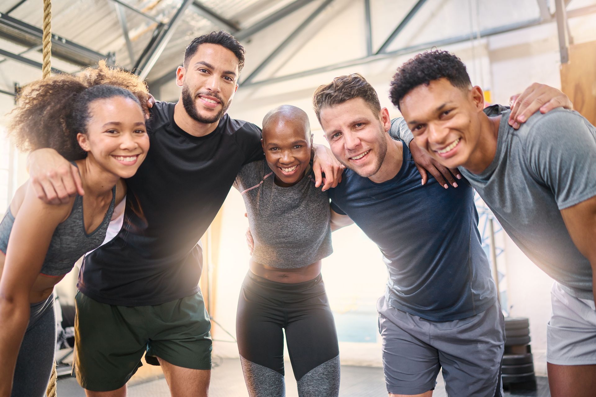 Five people in workout clothes, smiling and posing with arms around each other in a gym.