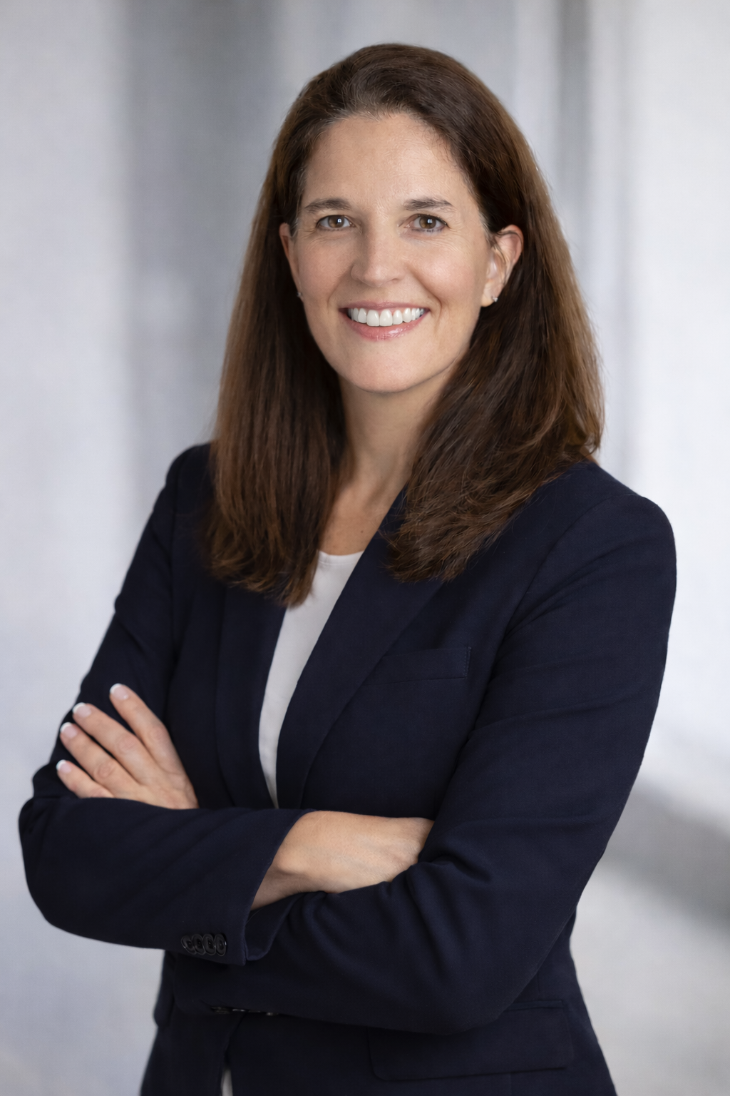 A woman with long brown hair is smiling and wearing a necklace