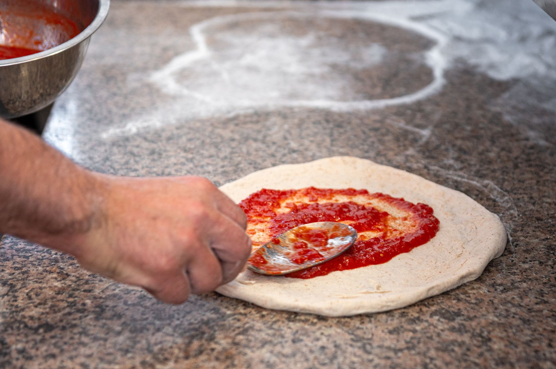 Una persona sta spalmando la salsa di pomodoro sull'impasto della pizza.