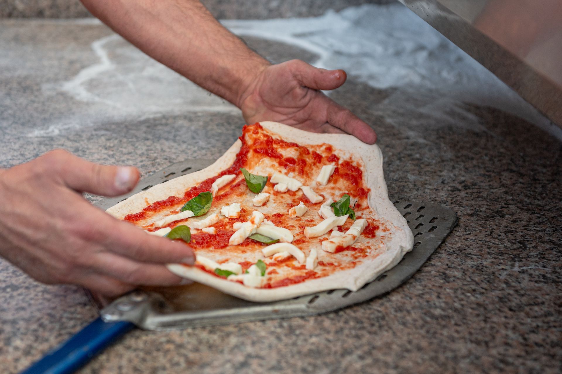 Una persona sta preparando una pizza con salsa di pomodoro e formaggio.