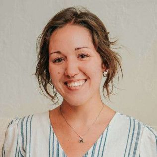 Woman with brown hair smiling, wearing a blue and white striped top, a necklace, and small earrings.