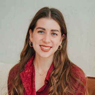 Woman with long brown hair, wearing a red shirt and gold earrings, smiles at the camera.