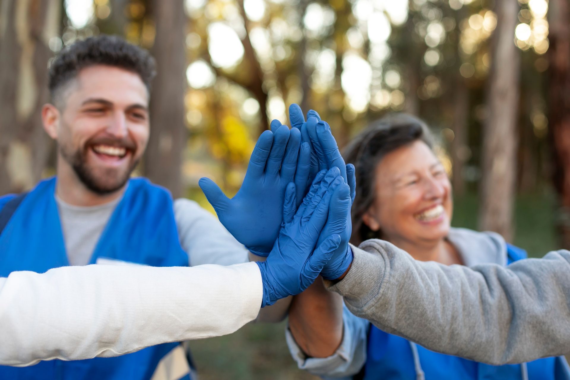 Group of volunteers in blue vests giving a high-five, smiling in a park.