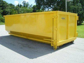 A bright yellow rectangular roll-off dumpster sitting on a paved surface outdoors with trees in the background.