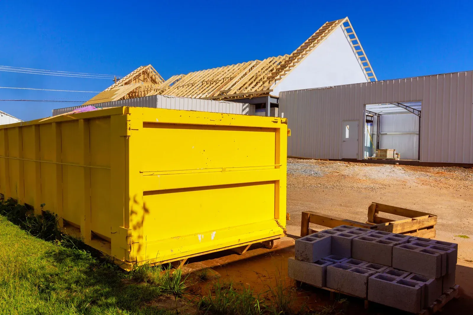 A large yellow construction dumpster sits in front of a building under construction with concrete blocks nearby.