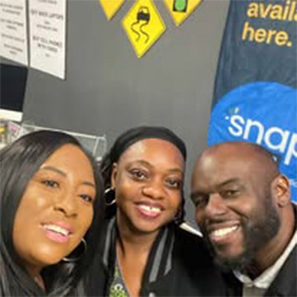 Three people are posing for a picture in front of a sign that says snap.