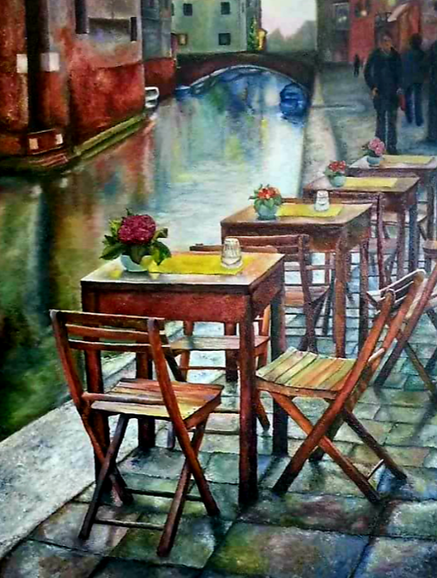 Tables and chairs set for diners on a canal-side walkway; a bridge, water, and buildings are in the background.