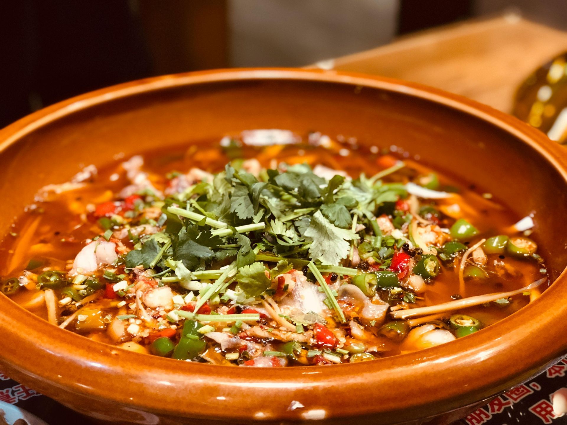 Spicy fish soup in a brown clay pot, topped with cilantro and green peppers.
