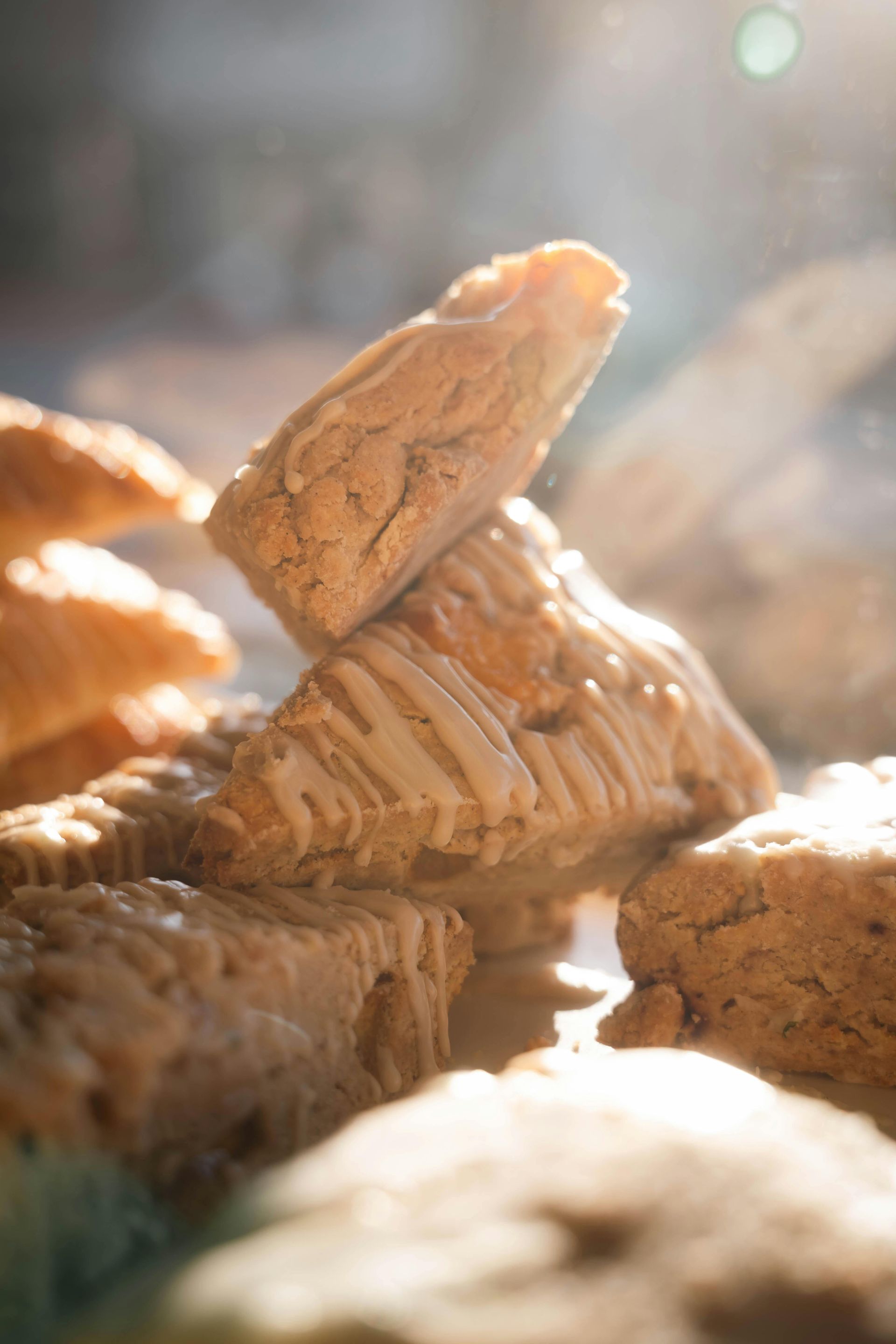 Pile of light-brown, glazed scones in soft focus, catching the sunlight.