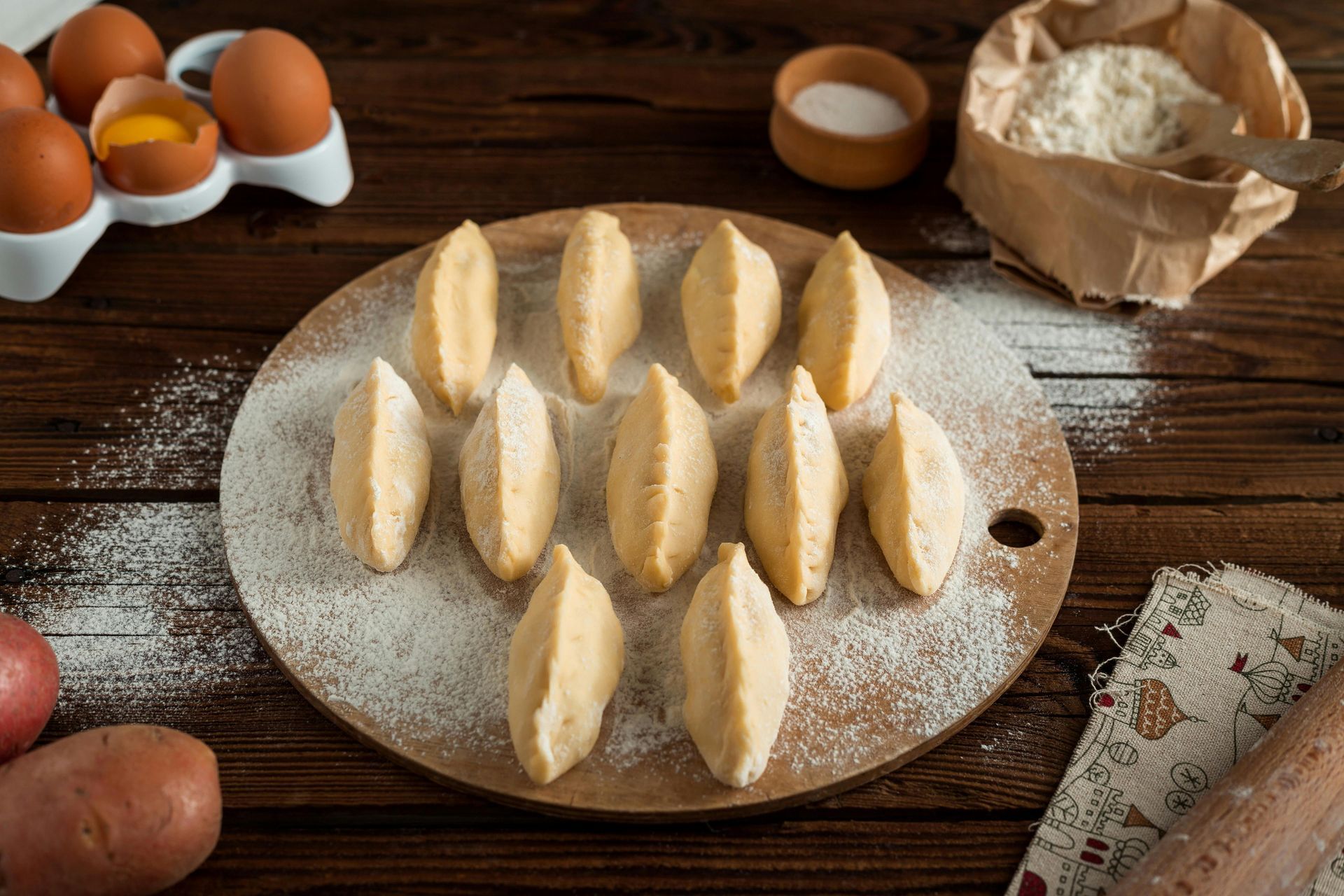pierogi arranged on a wooden board sprinkled with flour, ingredients nearby: eggs, flour, salt.