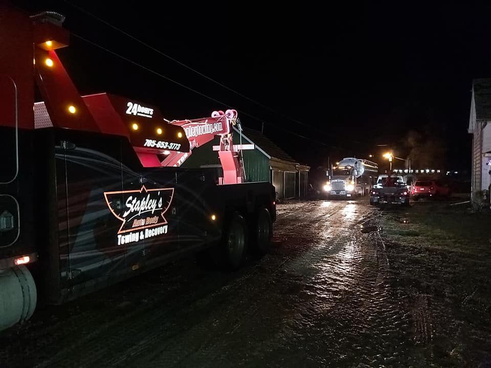 Tow trucks on a dark, wet street at night; one is loading a vehicle.
