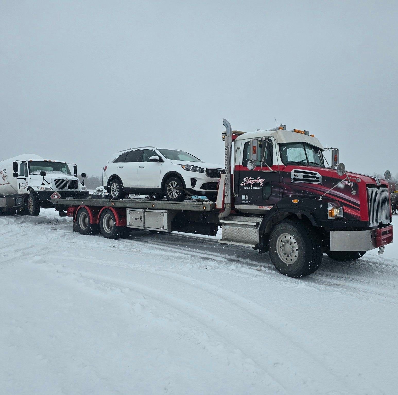 A white SUV is being towed by a flatbed tow truck on a snowy day.
