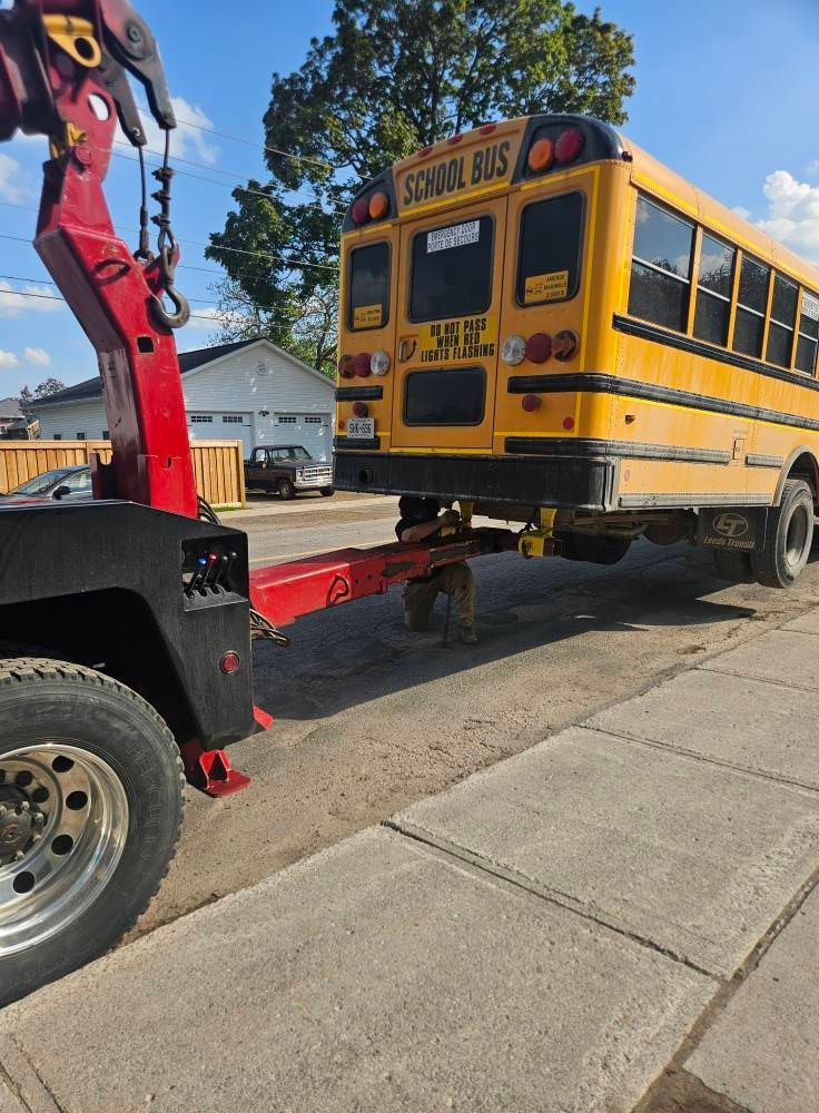Tow truck towing a yellow school bus on a paved road; sunny day.
