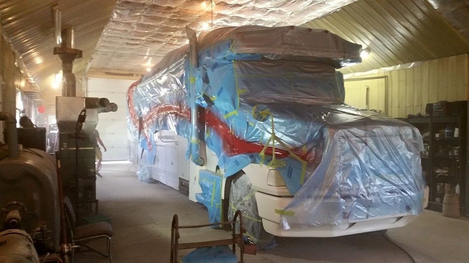 RV covered in blue plastic, inside a garage, being painted.