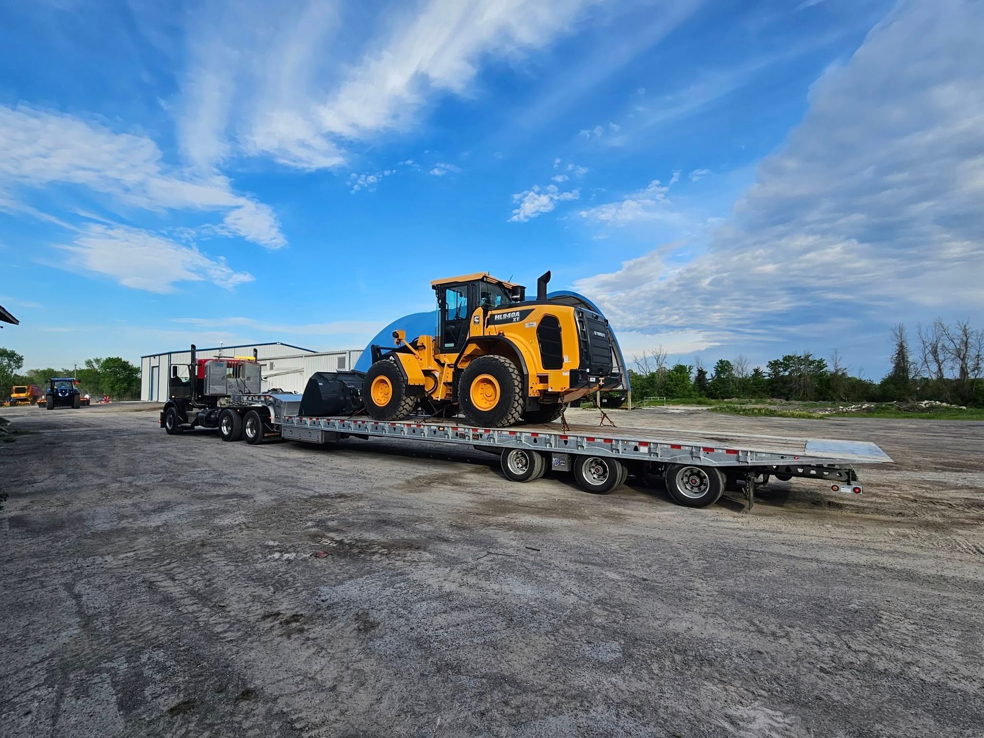 Yellow construction vehicle loaded on a flatbed trailer under a blue sky.