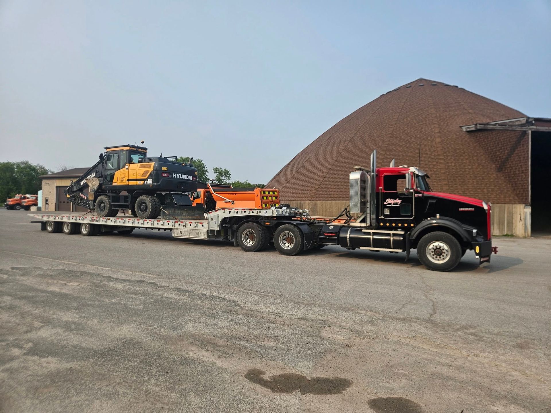 Black and red semi-truck hauling heavy construction equipment on a flatbed trailer.