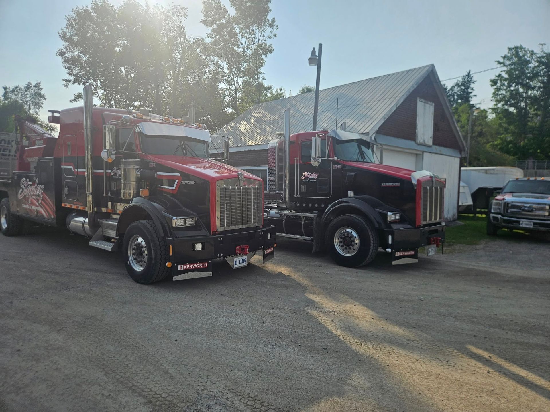 Two red and black tow trucks parked outside a building on a gravel lot.