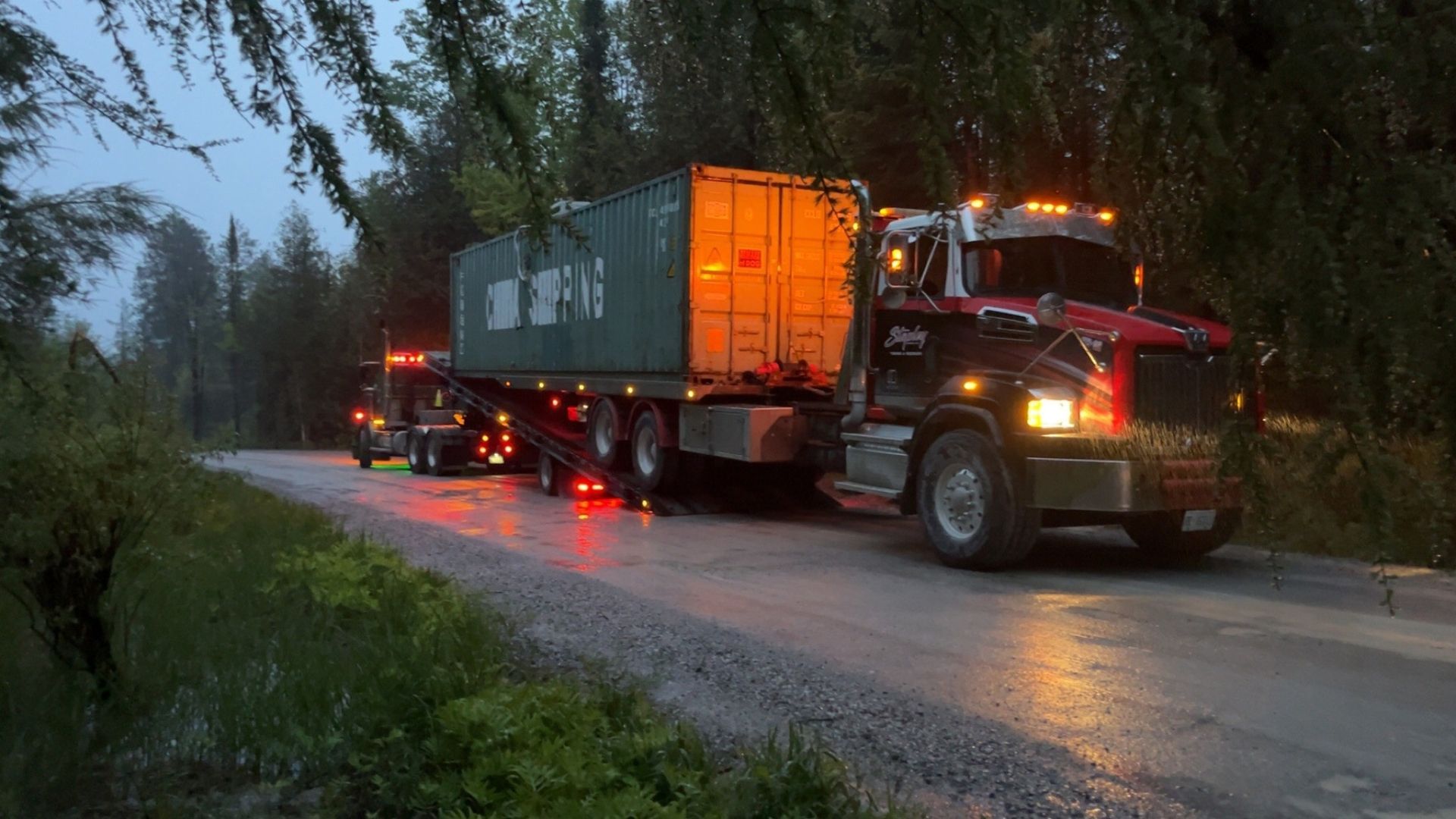 Semi-truck hauling container on a wet road, lit by headlights and taillights.  Green container, dark truck.