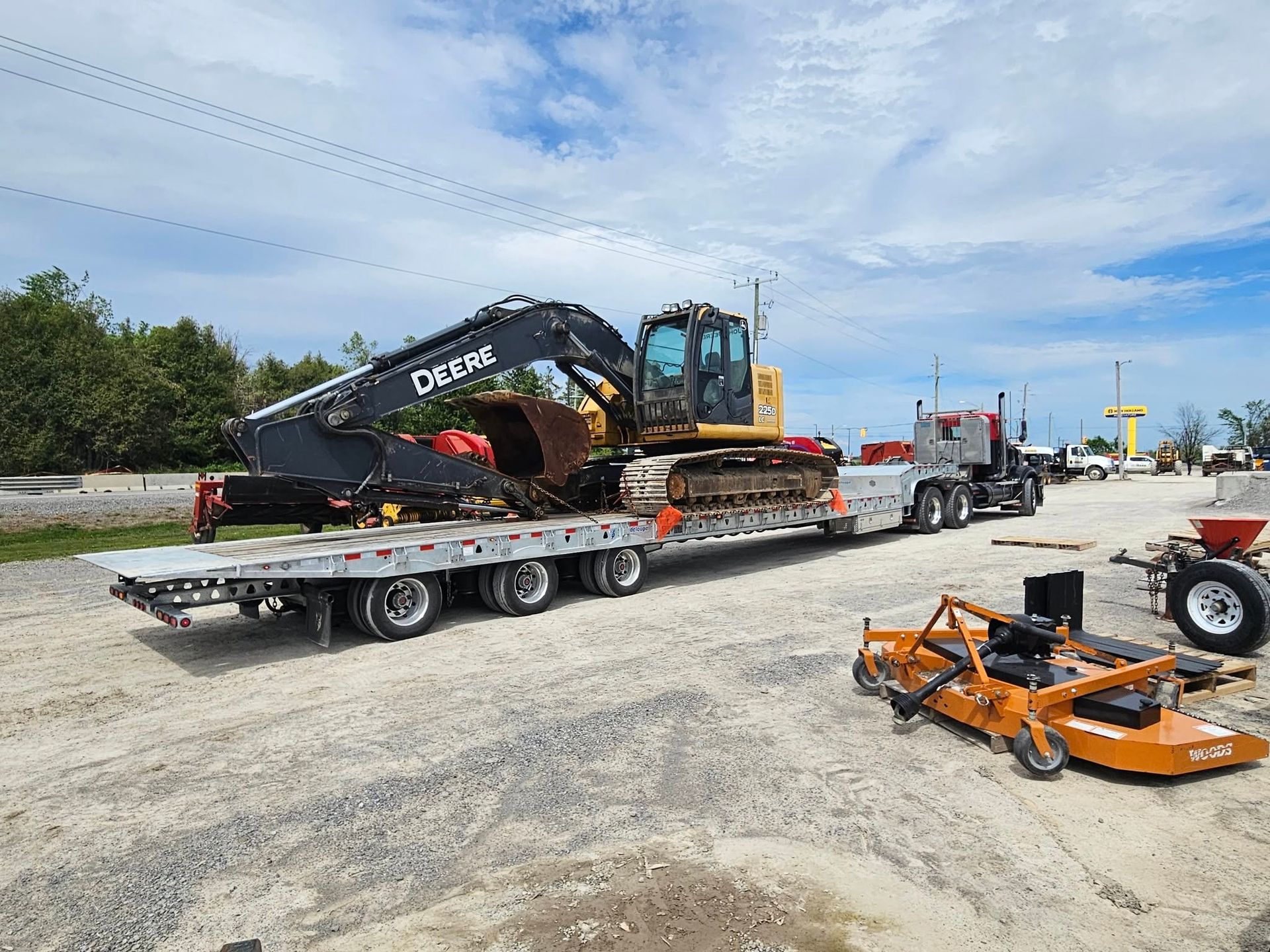 Excavator on a trailer being hauled by a semi-truck in an outdoor setting.