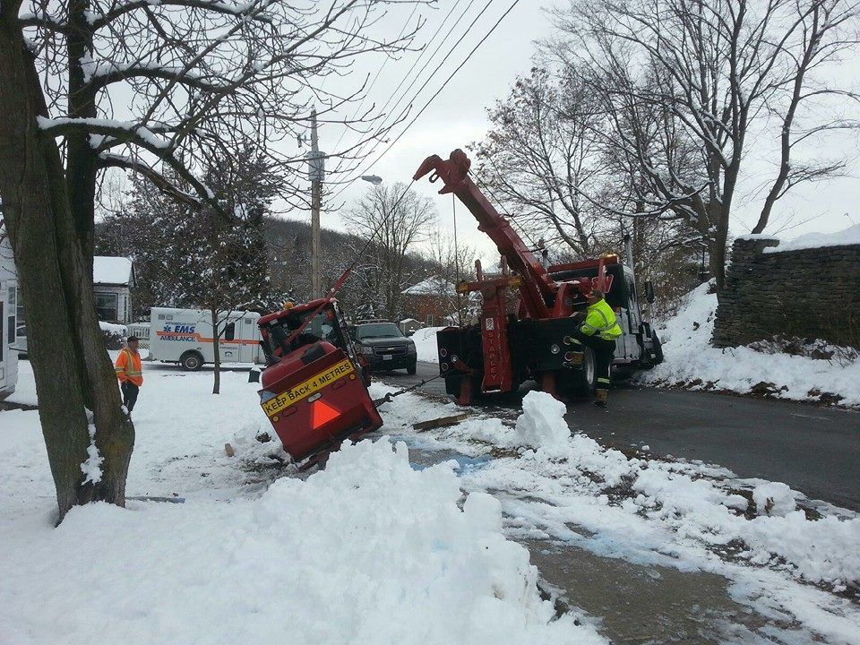 A tow truck attempting to extract a smaller vehicle from snow on a road.