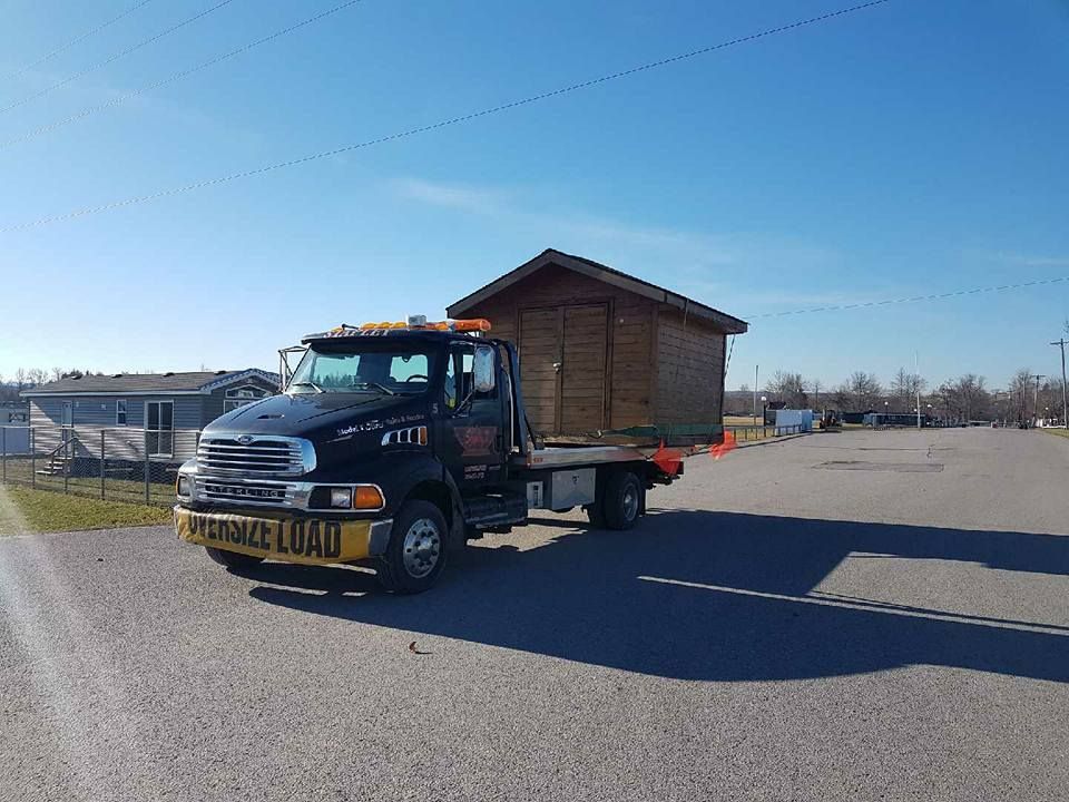 Truck transporting a small wooden building on a sunny day. 