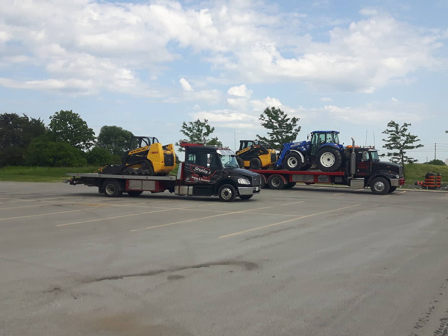 Two trucks with construction equipment parked in an asphalt lot under a cloudy sky.