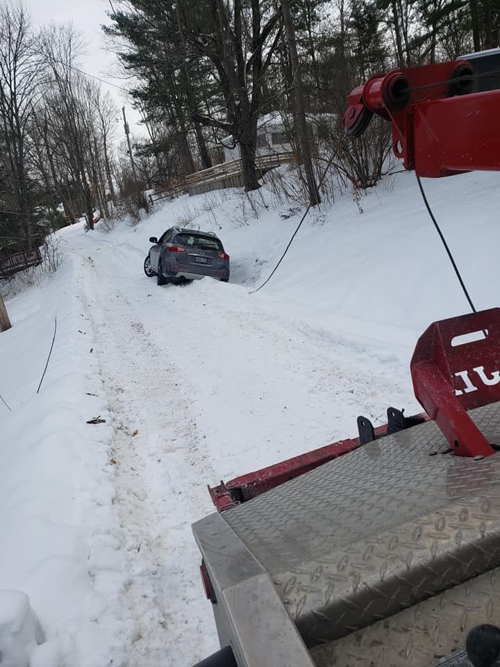 A tow truck pulling a car stuck in a snow-covered driveway.