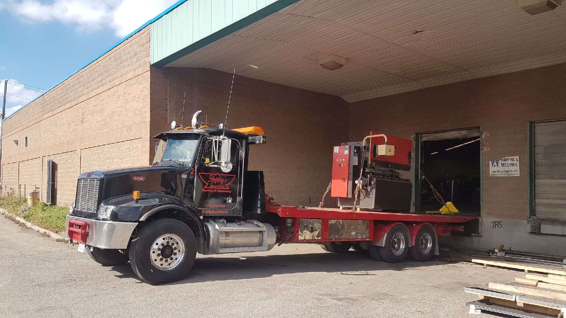 Black flatbed truck parked near a loading dock; red equipment on the bed.