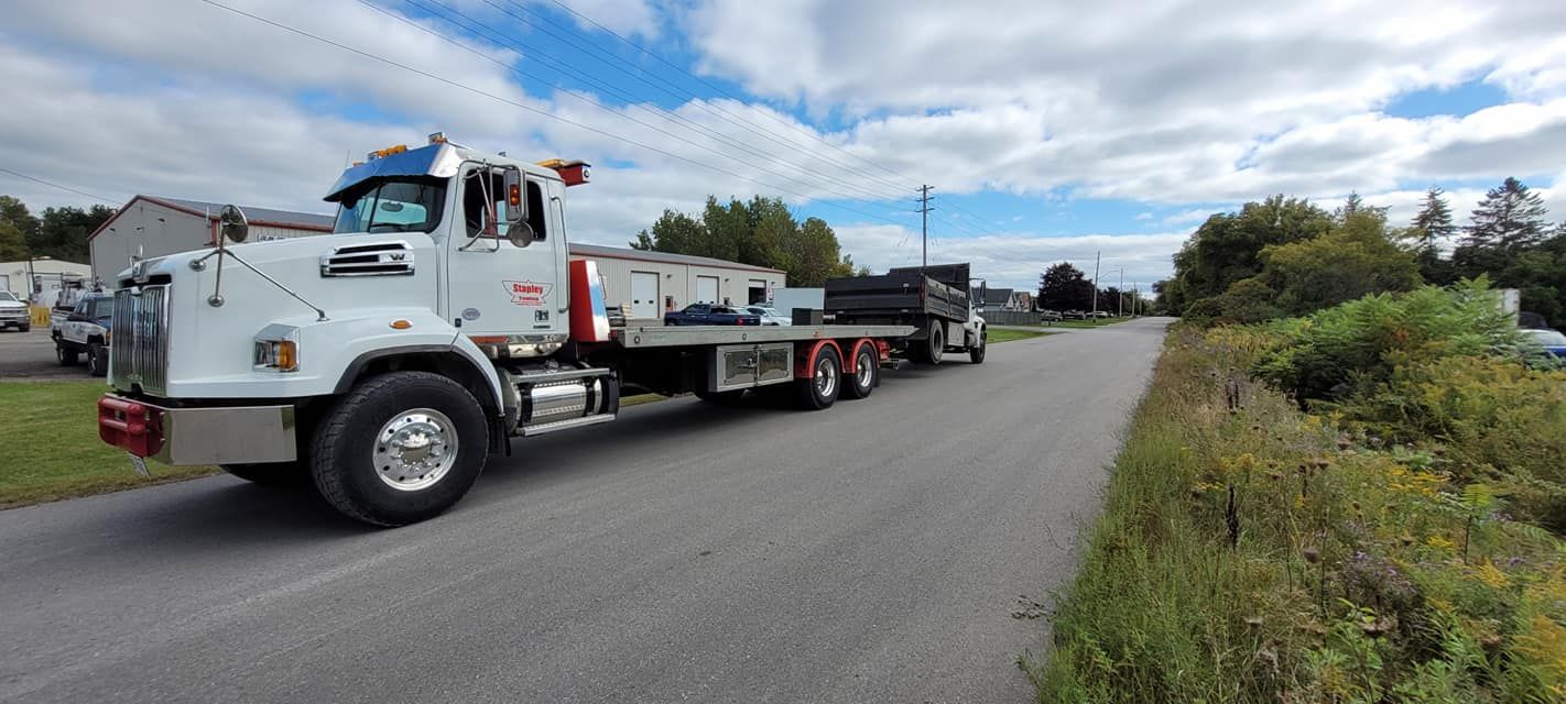 A white semi-truck with a flatbed trailer on a road, cloudy sky.