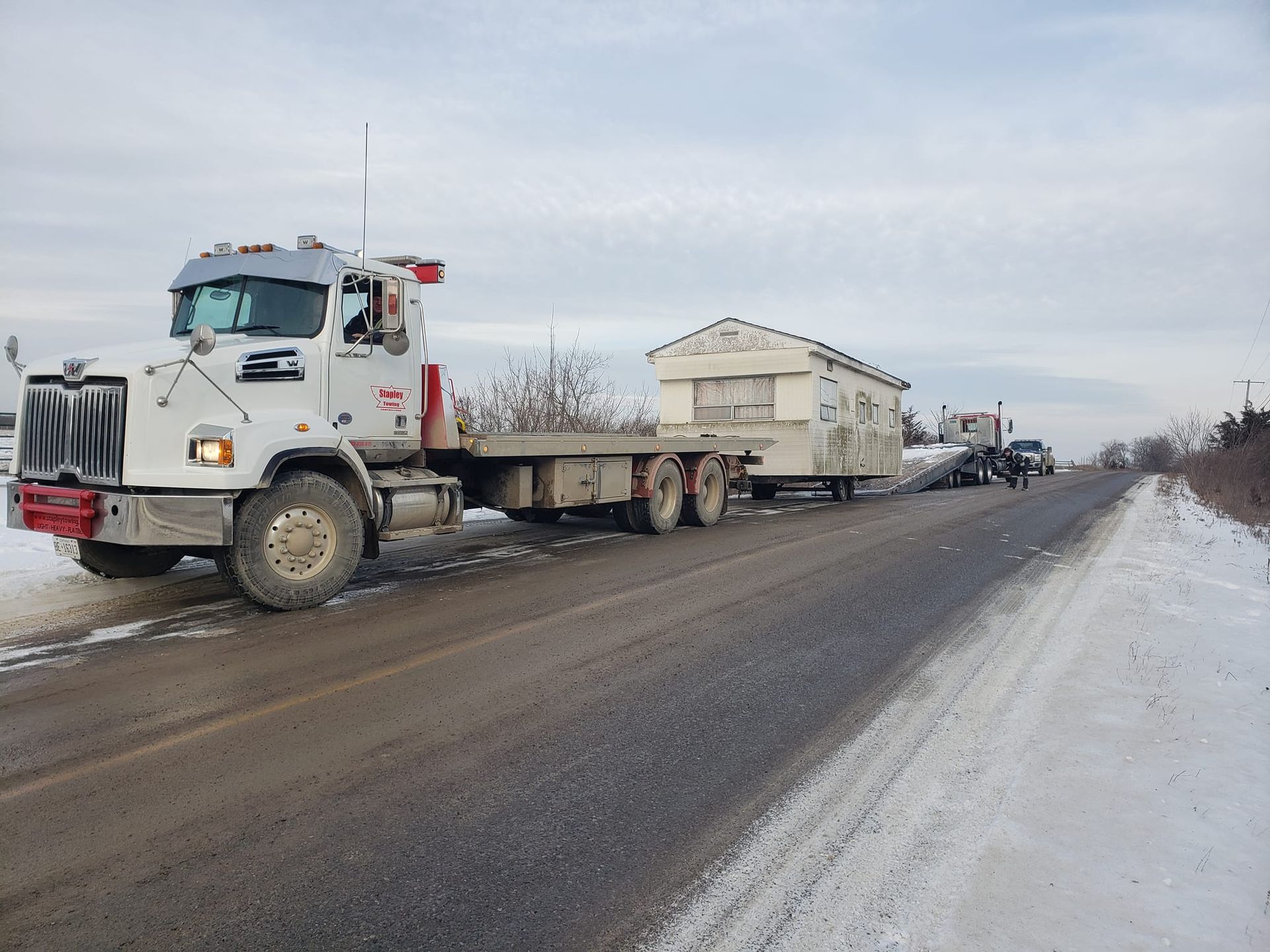 A large truck transporting a modular home on a snowy roadside.