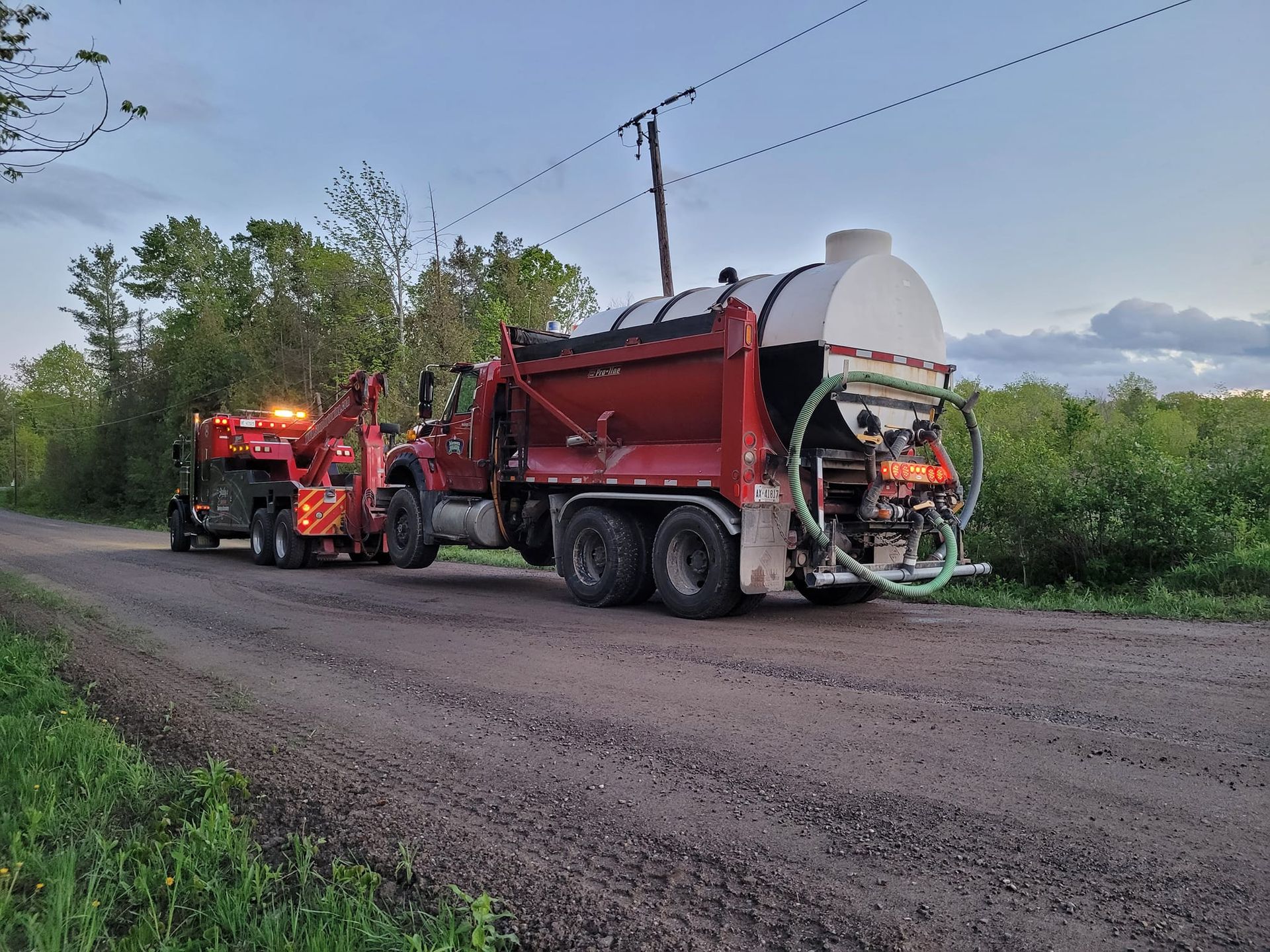 Red truck and trailer on a gravel road, likely for road maintenance.