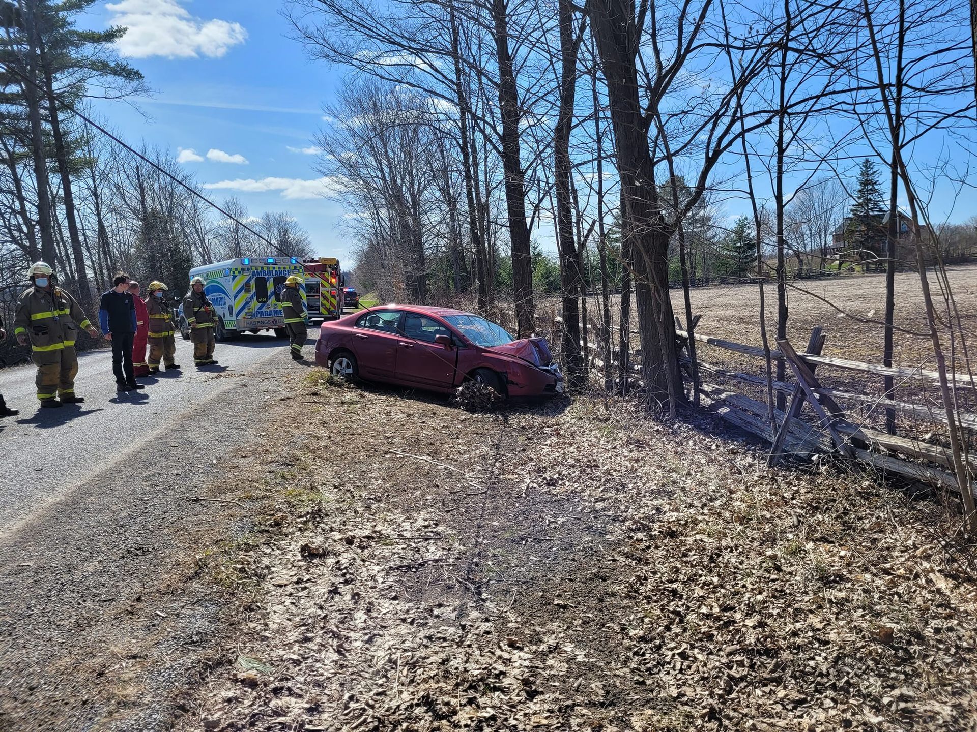 Car crashed into trees beside a road. Emergency responders and ambulance present.