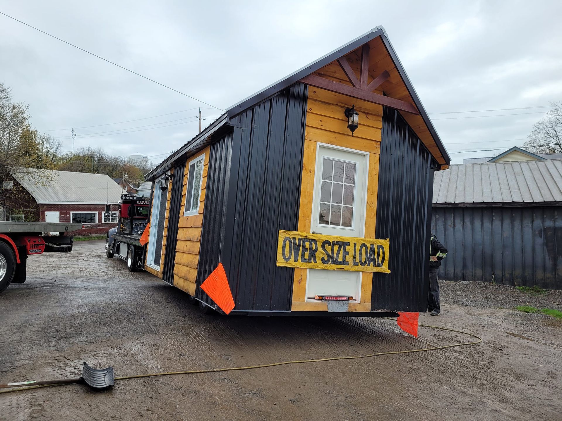 Tiny house on a trailer, black exterior, orange safety flags. 