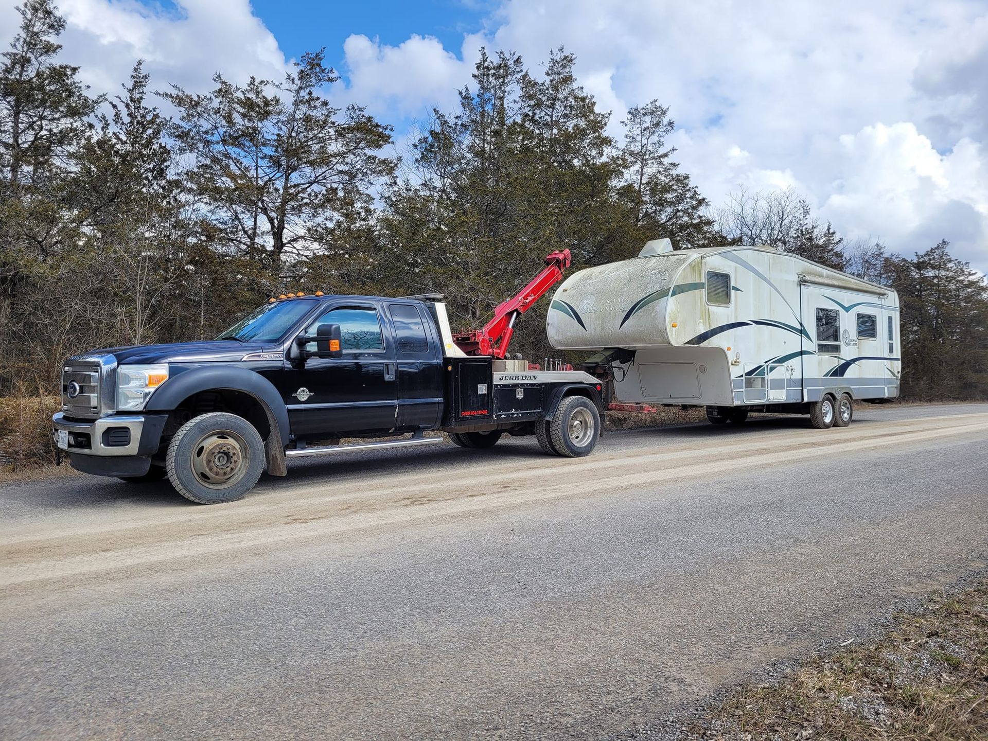 Black tow truck towing a white RV on a gravel road, under a cloudy sky.