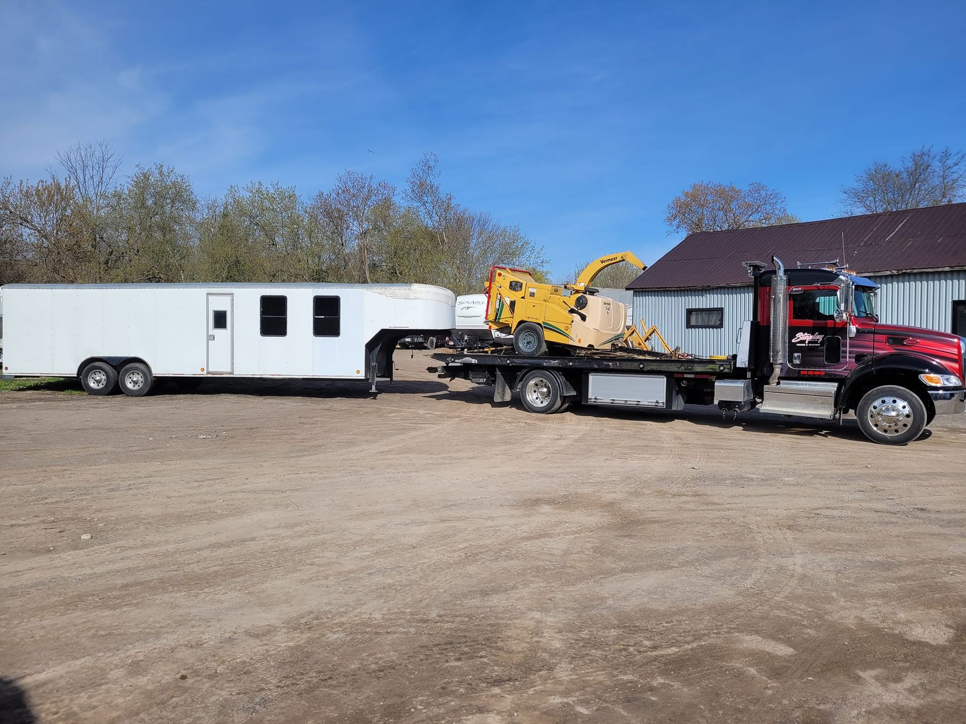 Truck towing a trailer and a yellow construction machine on a flatbed, parked outdoors.