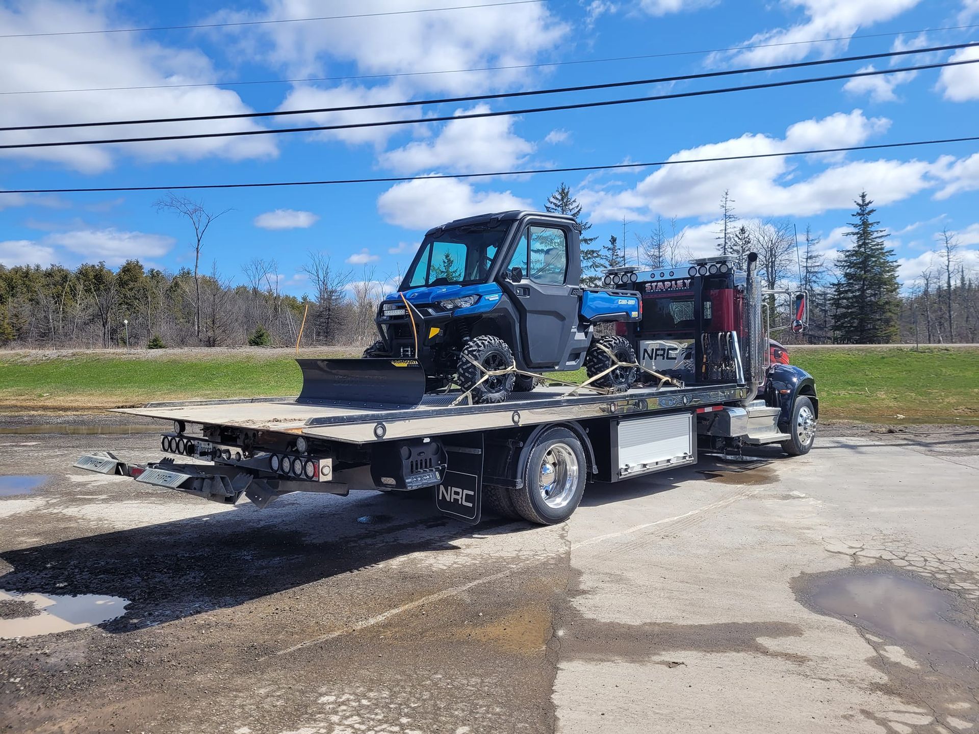 A blue ATV on a flatbed tow truck outdoors on a sunny day.