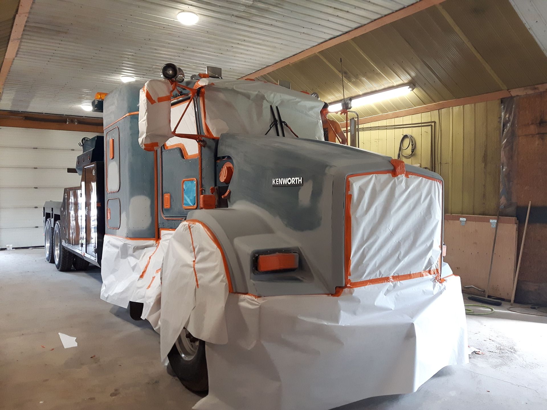 Gray semi-truck covered in white paper, taped with orange, inside a garage.