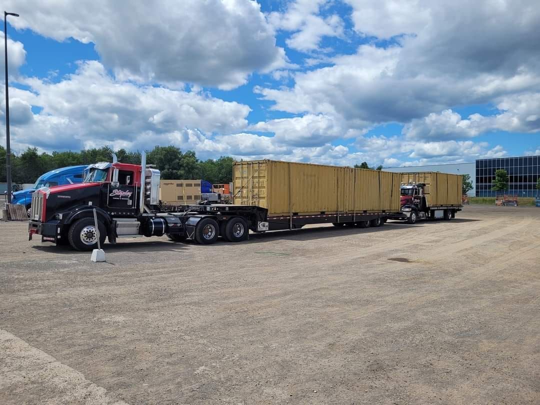 Black and red semi-truck pulling a long line of yellow shipping containers on a gravel lot under a cloudy sky.