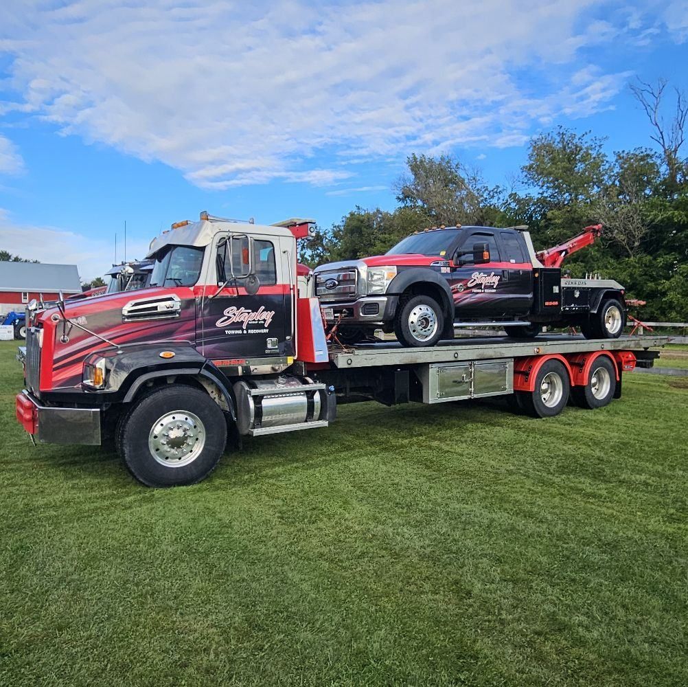 Tow truck with a black pickup truck on its flatbed, on green grass under a blue sky.