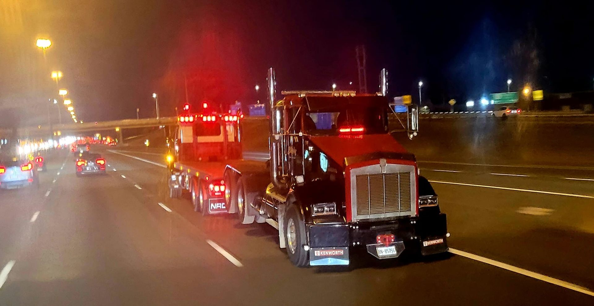 Two semi-trucks with flashing lights traveling on a highway at night.