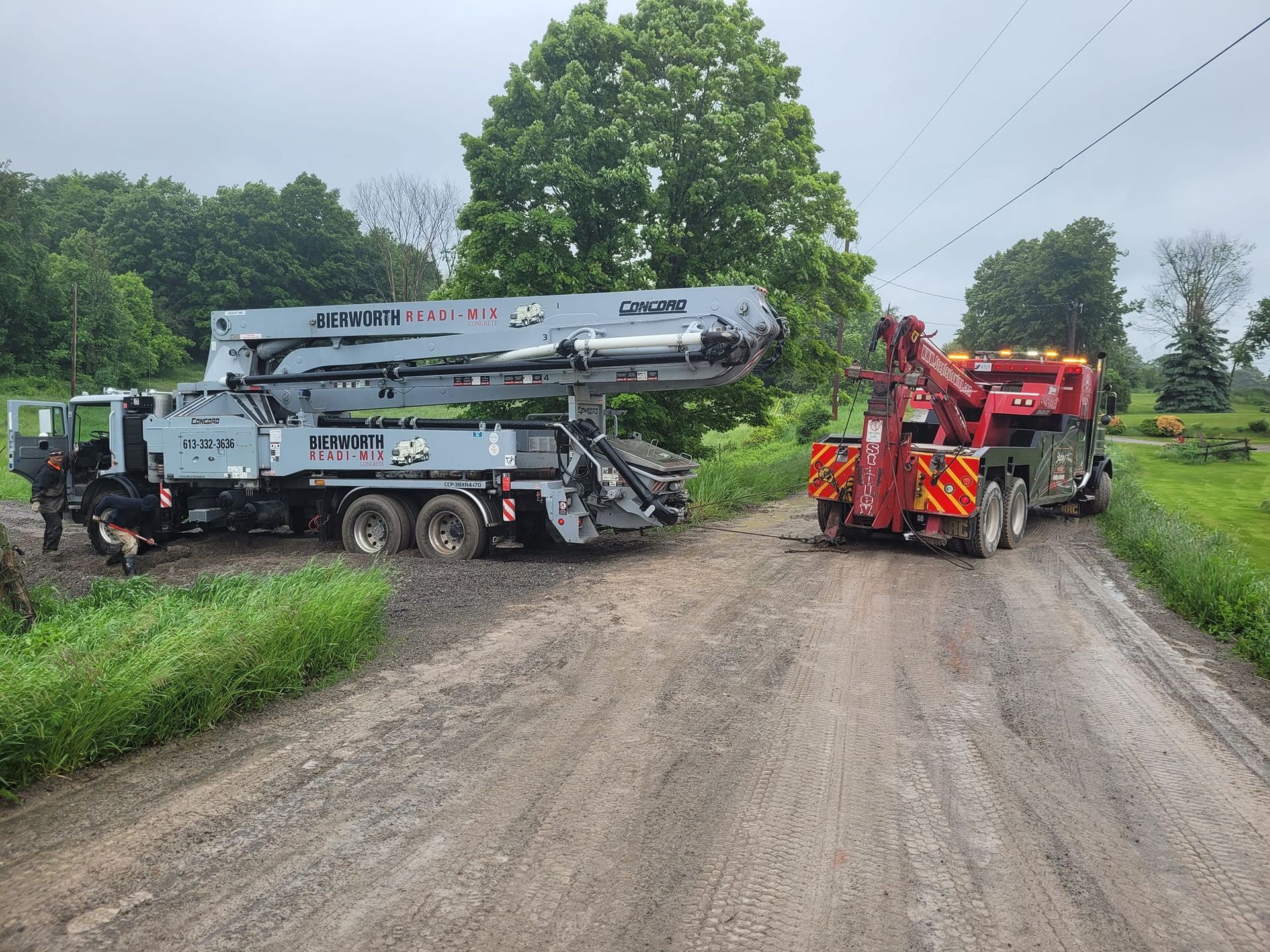 Tow truck assisting a large gray boom truck on a muddy road.