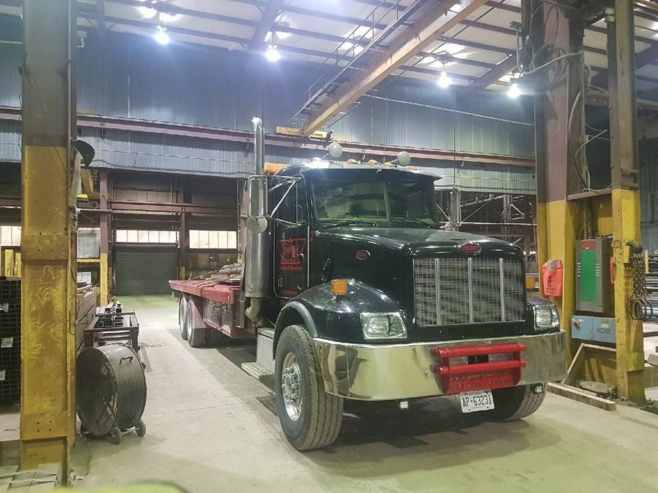 Black semi-truck with flatbed inside a warehouse; silver bumper, red guard, tall exhaust stacks.
