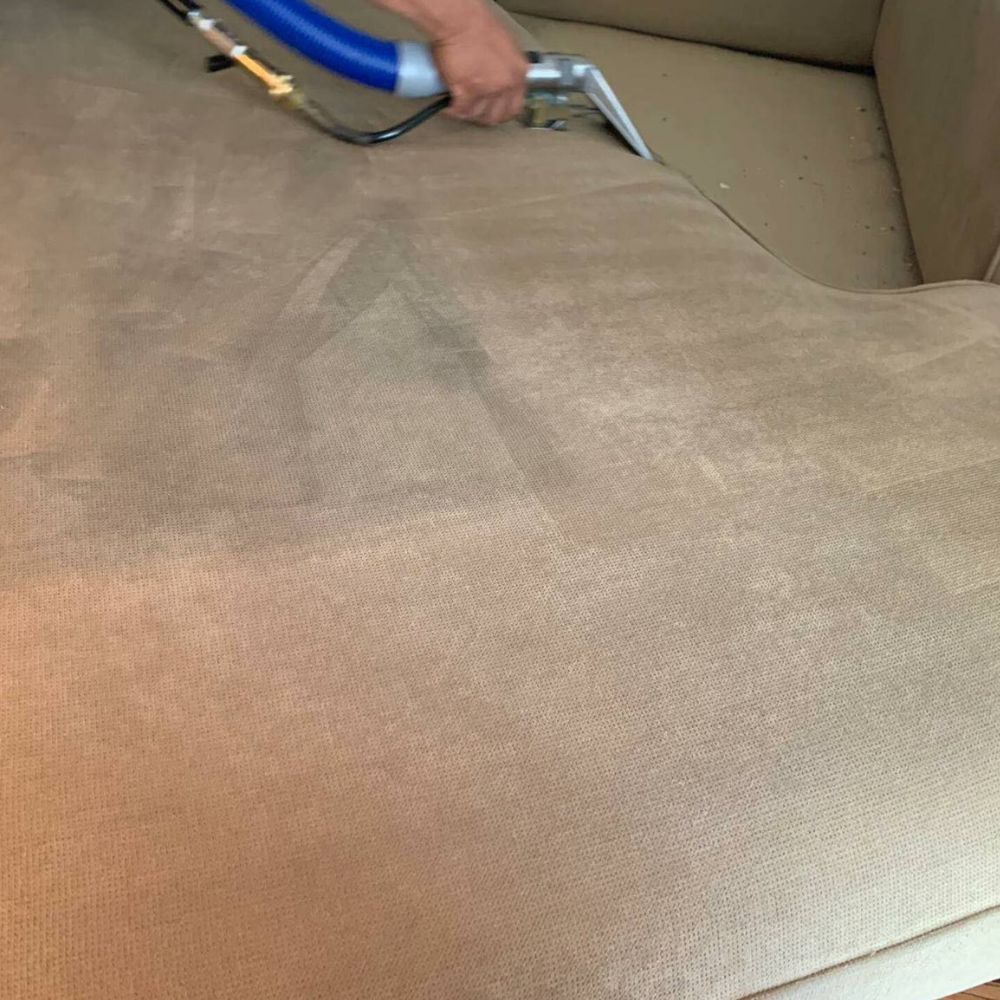 A person is cleaning a couch with a vacuum cleaner.