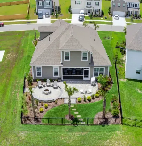Aerial view of a gray house with a backyard patio, fire pit, palm trees, and green grass.