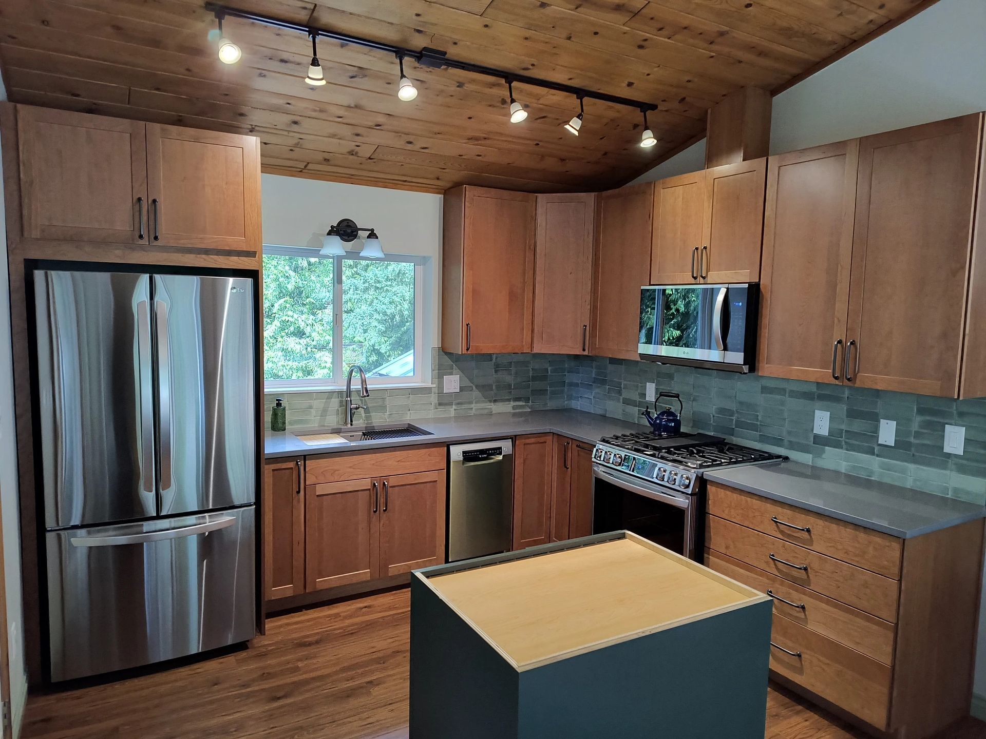 Modern kitchen with wood cabinets, stainless steel fridge, granite counters, and a central island under track lighting