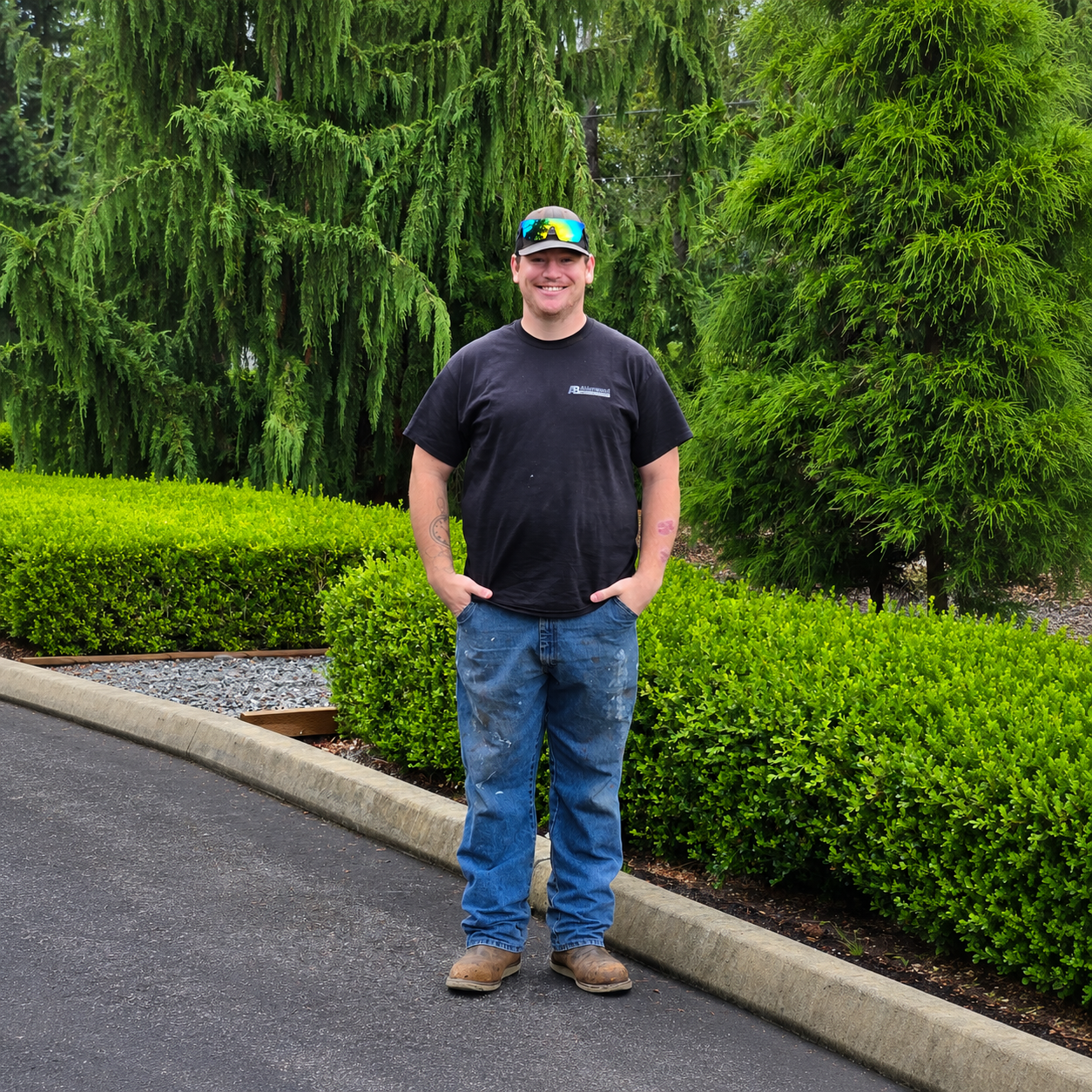 Smiling person in a black hoodie and camo cap standing on a wooden deck outdoors