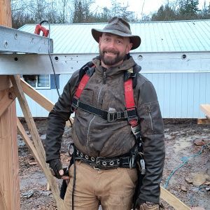 Construction worker in hard hat and harness standing outdoors beside a metal building frame