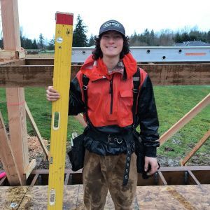 Person in red jacket holding a yellow level at a construction site outdoors.