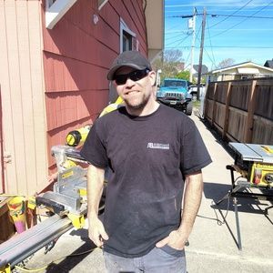 Smiling person in a black hoodie and camo cap standing on a wooden deck outdoors
