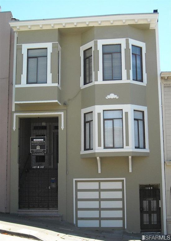 Three-story beige building with white trim, bay windows, garage, and a gated entrance.